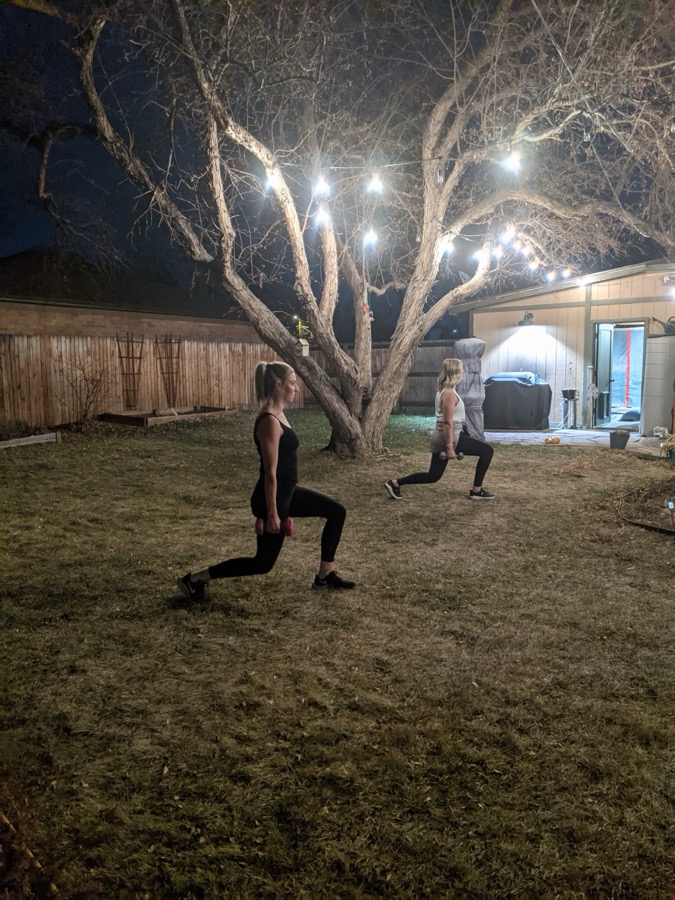 Two clients doing dumbbell lunges in a backyard under string lights