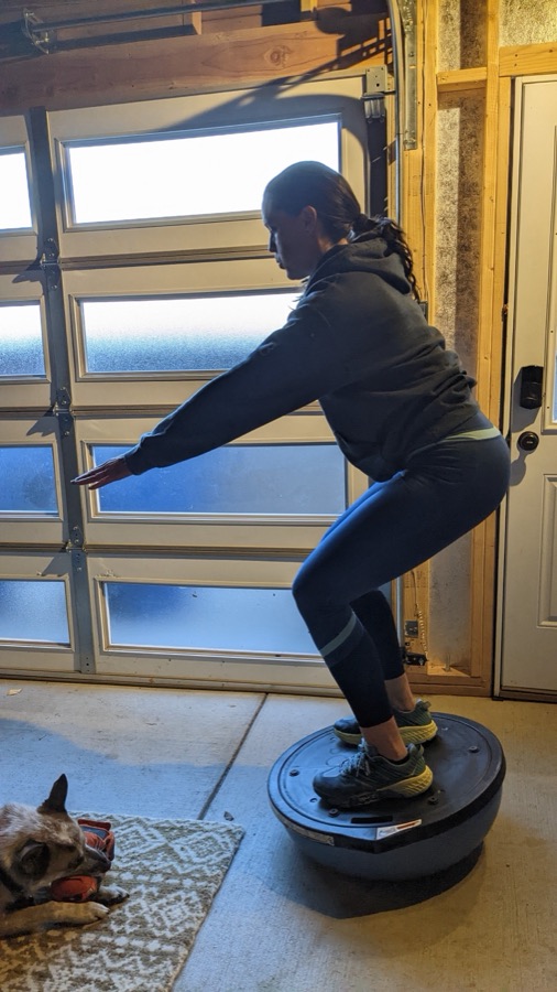 Client holding a squat on a BOSU ball in a garage gym