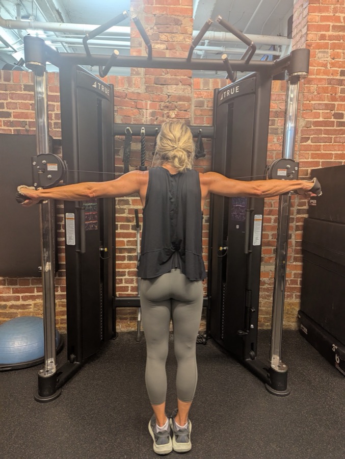 Client working through cable raises at the functional trainer in a brick gym